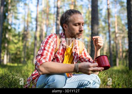 Middle aged man eating berries in green nature. Thoughtful European male with mug in hand at forest Stock Photo