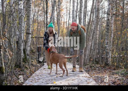 Happy family couple dog owners playing together with dog walking in autumn Scandinavian park. Stock Photo