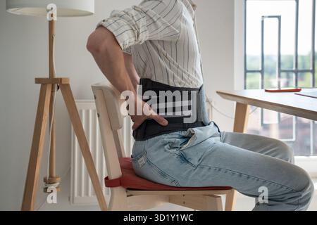 Man wearing back support belt on lower back during exacerbation to treatment of hernia. Stock Photo
