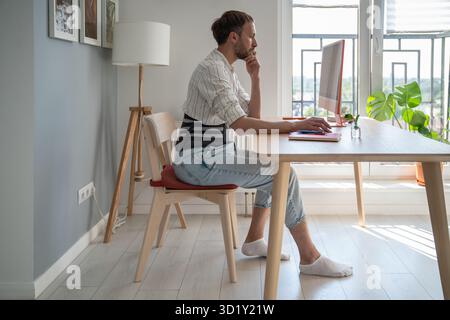 Young man freelancer wearing back brace sitting at table using computer Stock Photo