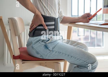 Man freelancer wearing back support belt working remotely from home Stock Photo