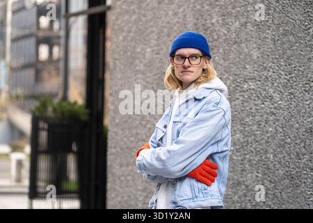 City portrait of stylish guy with arms crossed, standing near wall, waiting, looking into distance Stock Photo