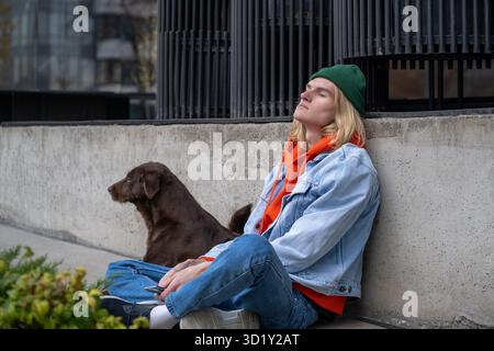 Depressed guy sitting on ground unhappy because of broken relations. Street dog supports lonely male Stock Photo