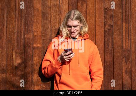 Smiling blonde man use smartphone outside, looks at phone screen, checking mobile apps, social media Stock Photo
