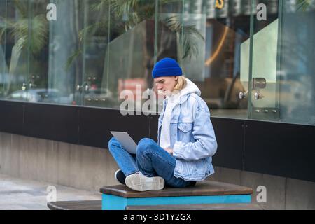 Hipster guy in trendy outwear sitting in street, working freelance online, messaging in internet Stock Photo