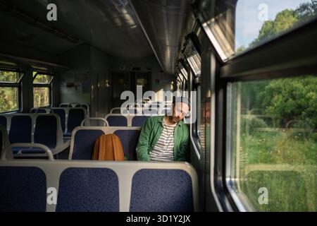 Sleepy man worn out from demanding workday, naps on an empty train ride home. Early rise, exhaustion Stock Photo