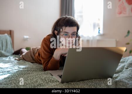 Interested teen girl spending weekend, pastime at home, watching video, film on laptop computer Stock Photo