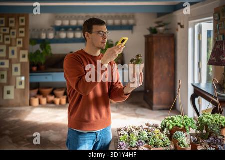 Young man choosing plant in store by making photo, reading information in mobile application Stock Photo