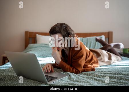 Concentrated teen girl reading book online, scrolling social networks in internet on laptop computer Stock Photo