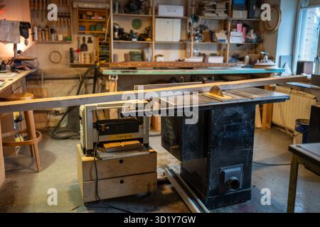 Tablesaw on workbench in carpentry workshop, shelves with tools and wood planks for furniture make Stock Photo