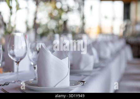 A beautiful table is prepared for guests in a modern restaurant. White napkins are neatly folded on plates, and glasses are lined up, suggesting an up Stock Photo