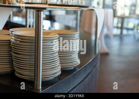 In a contemporary event setting, neatly stacked white plates await guests. The elegant table design and bright lighting create an inviting atmosphere Stock Photo