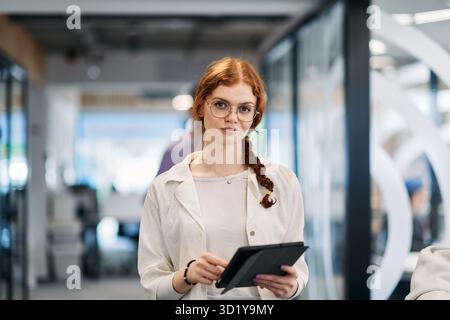 A business woman with orange hair self confident, fully engaged in working on a tablet, exuding creativity, ambition and a livel Stock Photo