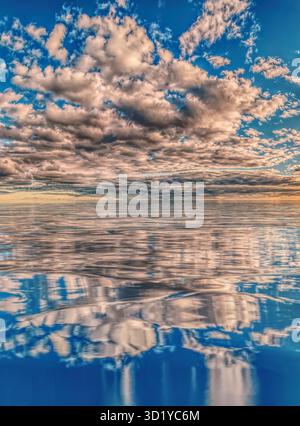 Warm sunset colours reflect off a serene ocean of calm water and a sky alive with dramatic clouds Stock Photo