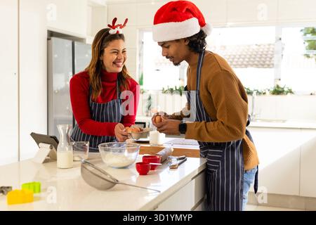 Couple wearing festive hats preparing baking ingredients at kitchen island with tablet Stock Photo