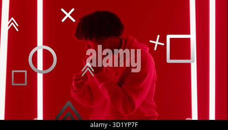 Standing man adjusting headphones in red-lit studio, wearing hoodie with neon strips and overlays Stock Photo