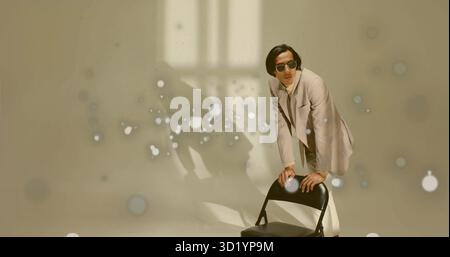 Man in beige suit leaning on black folding chair in studio, sunglasses, light spots, copy space Stock Photo