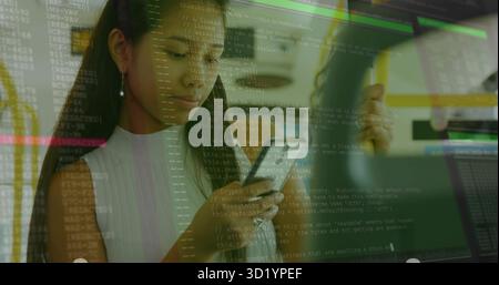 Reviewing smartphone screen, female developer at tech workstation with monitors displaying UI code Stock Photo