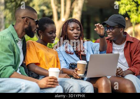 African American friends enjoying movie and video call on laptop in park, laughing on weekend walk Stock Photo