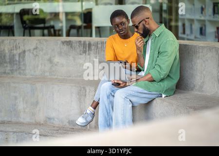 Focused African American multiracial couple work on laptop outdoors, prepare for exams, remote study Stock Photo