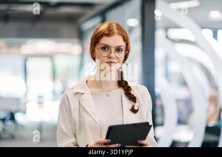 A business woman with orange hair self confident, fully engaged in working on a tablet, exuding creativity, ambition and a livel Stock Photo