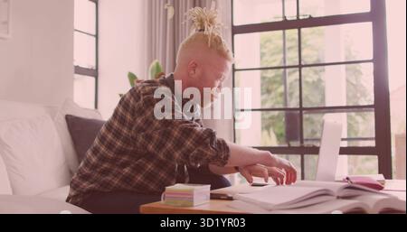 Studying man wearing flannel shirt organizing notes in living room with laptop, books, headphones Stock Photo