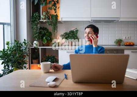 Relaxed smiling woman enjoy morning tea, consulting clients on phone. Freelancer working on calls Stock Photo