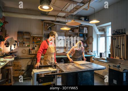 Carpenter man supervising novice woman working on circular saw table in woodworking workshop Stock Photo