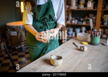 Woman potter hands shaping white clay bowl at wooden candle lit table in pottery workshop studio Stock Photo