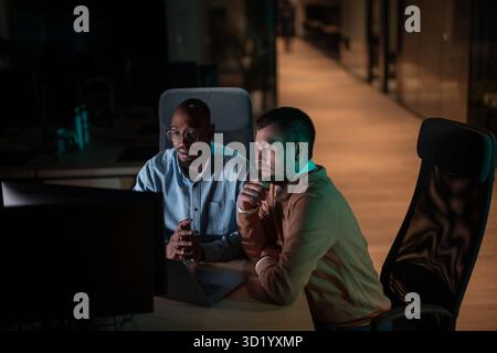 Focused multicultural team collaborating late at night, analyzing data and strategy. Concepts of teamwork, productivity, and bus Stock Photo