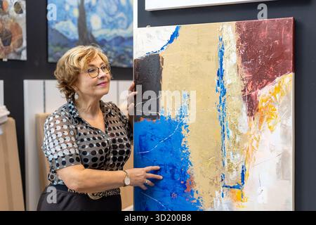 An art lover stands near a vibrant abstract painting, admiring its colors and textures at a local gallery during a lively art exhibition. The atmosphe Stock Photo