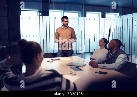 A diverse team of young professionals collaborates in a modern office conference room. Businesspeople discuss strategy, technolo Stock Photo