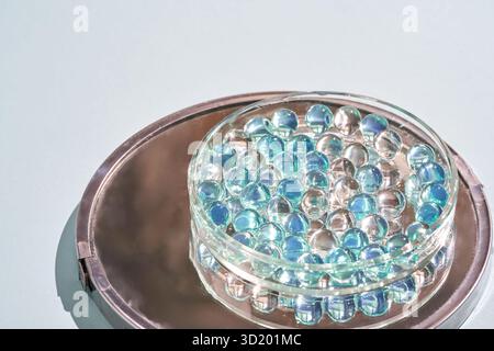 Glass marbles in transparent dish on metal tray with light blue background. Stock Photo