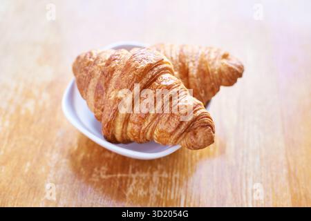 Golden croissants on white plate - freshly baked pastries on wooden table Stock Photo