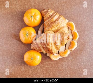 Delicious fresh croissants with vibrant oranges and sliced tangerines on wooden Stock Photo