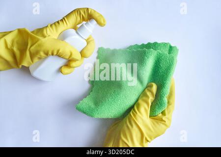 Hands in yellow gloves cleaning with spray bottle and green cloth on white Stock Photo