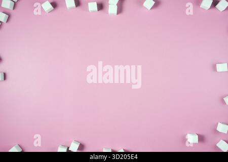 White sugar cubes scattered on pink background with empty space in center Stock Photo