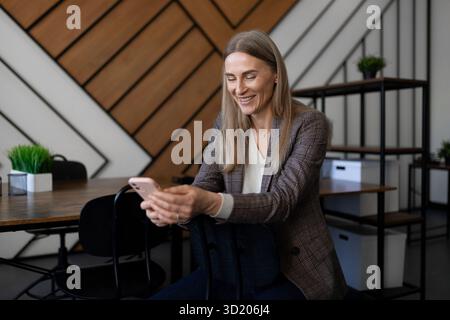 Professional woman smiling while using smartphone in modern office setting during daytime Stock Photo