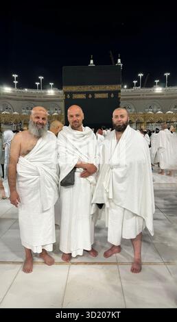 Three Muslim men in Ihram clothing standing in front of the Kaaba during Hajj or Umrah pilgrimage in Mecca, Saudi Arabia. Sacred Stock Photo