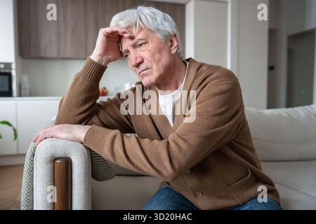 Lost sad elderly man with Alzheimer dementia sitting slumped on sofa, silent despair frustration Stock Photo