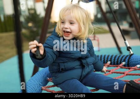 Child joyfully playing on a swing set in a modern playground during a sunny afternoon in a city park Stock Photo
