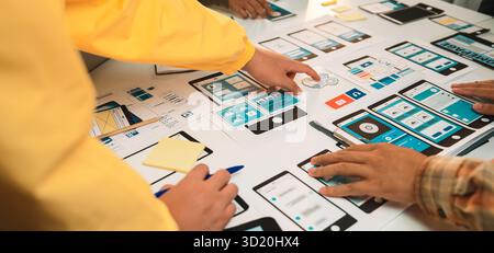 A vibrant workspace bustling with designers collaborating on a mobile app prototype, showcasing user interface wireframes, tools, and creative brainst Stock Photo