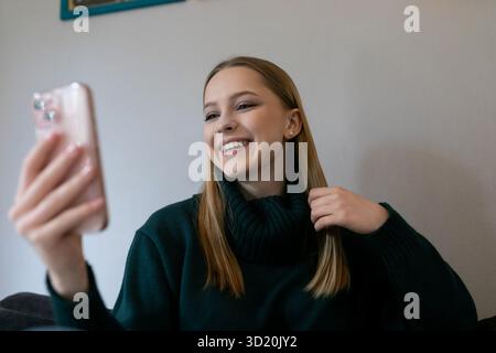 Young woman enjoying a virtual conversation while sitting on a couch in a cozy living room setting Stock Photo