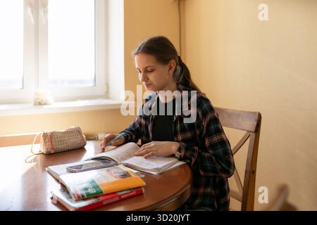 Teen studying at home in cozy setting while taking notes and using books during afternoon hours Stock Photo