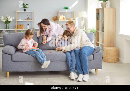 Happy family sitting on sofa inmodern living room, three generations of women are playing board game Stock Photo