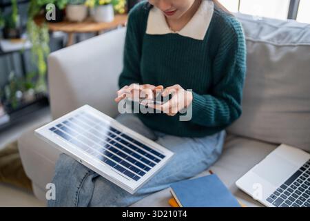 Asian Woman learning about renewable energy remote control of solar in her house and Installing solar panel sustainable technolo Stock Photo