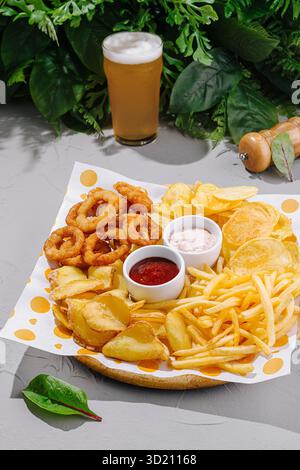 Delicious platter of crispy snacks including onion rings, fries, and potato chips with refreshing beer at a garden setting Stock Photo