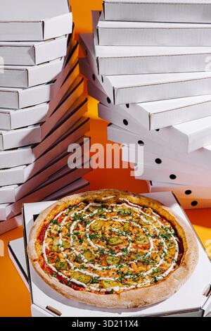Delicious pizza topped with vegetables and herbs placed in front of stacks of pizza boxes in a vibrant setting Stock Photo