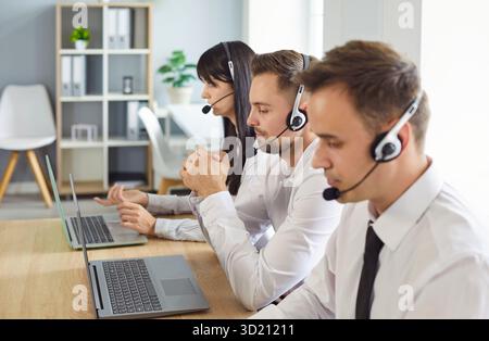 Focused support operators wearing headsets at desks with laptops in a office Stock Photo
