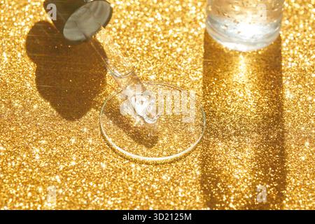 Sparkling gold glitter serum dropper on reflective surface with light reflection Stock Photo